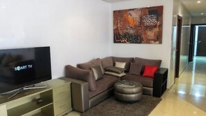 Un salon moderne avec un canapé d’angle, un téléviseur à écran plat et un élément décoratif mural.