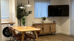 A modern kitchen with a dining area, a washing machine, and a large flat-screen TV.