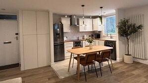 A modern kitchen with white cabinets, a stainless steel refrigerator, and a dining area with a wooden table and chairs.