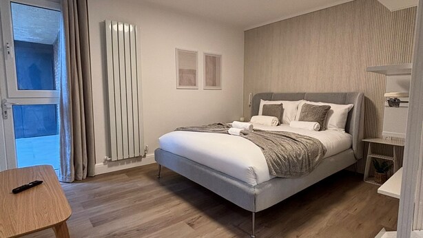 A modern bedroom with a bed, bedside table, and a window with curtains.