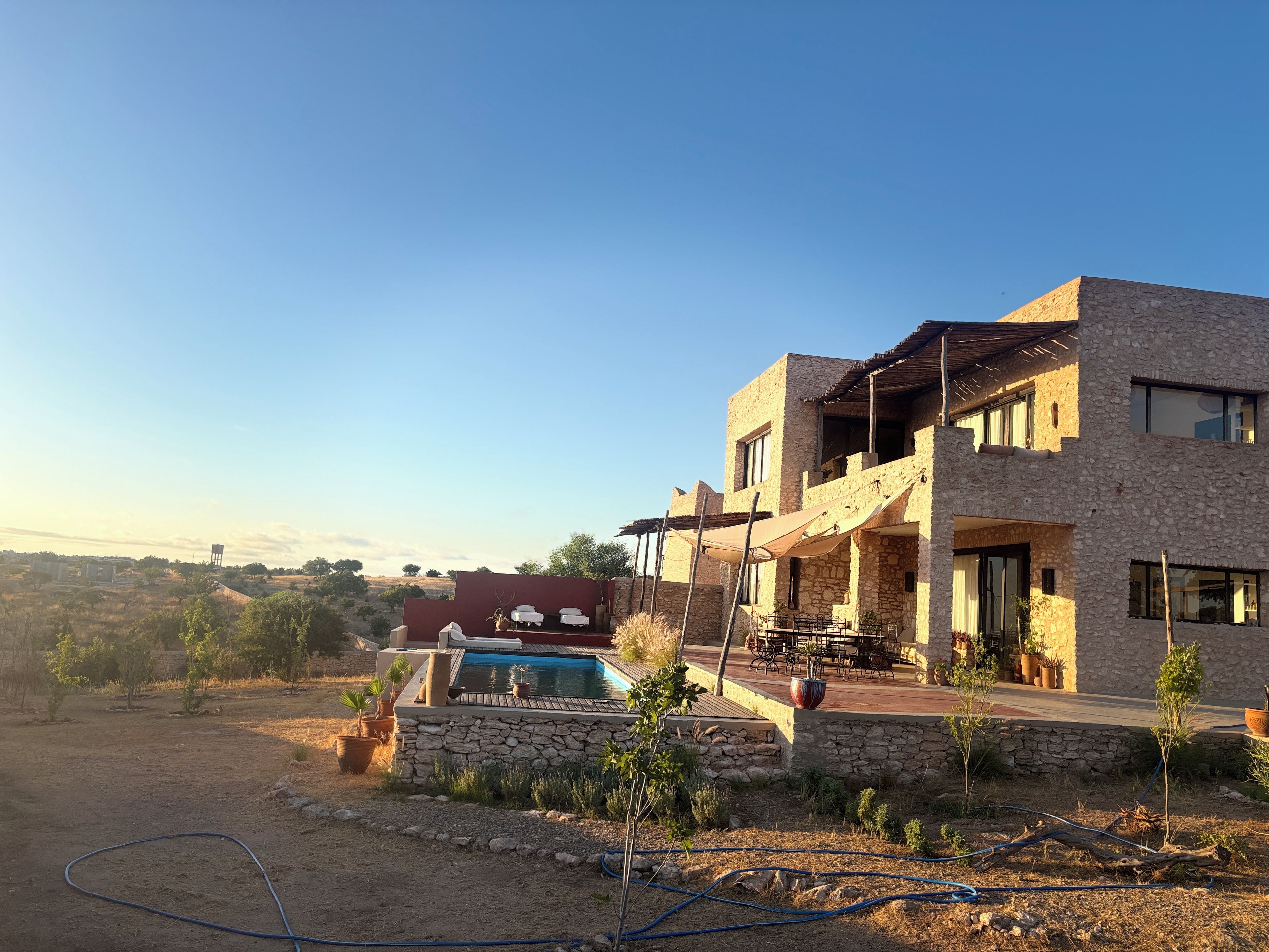 A modern two-story house with a stone facade, a swimming pool, and outdoor furniture.
