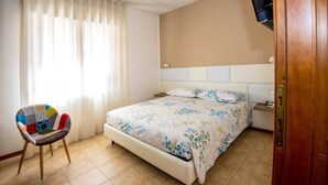 A hotel room with a bed, a chair, a television, and a window with curtains. - The Orchid - Francavilla al Mare (Francavilla al Mare)
