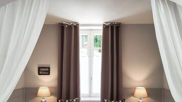 A bedroom with a large bed, two bedside tables with lamps, a window with curtains, and a picture on the wall.