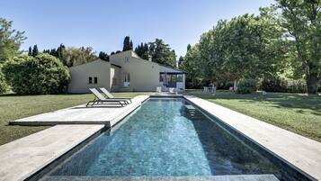 A rectangular swimming pool with clear water, surrounded by a wooden deck and a grassy lawn.