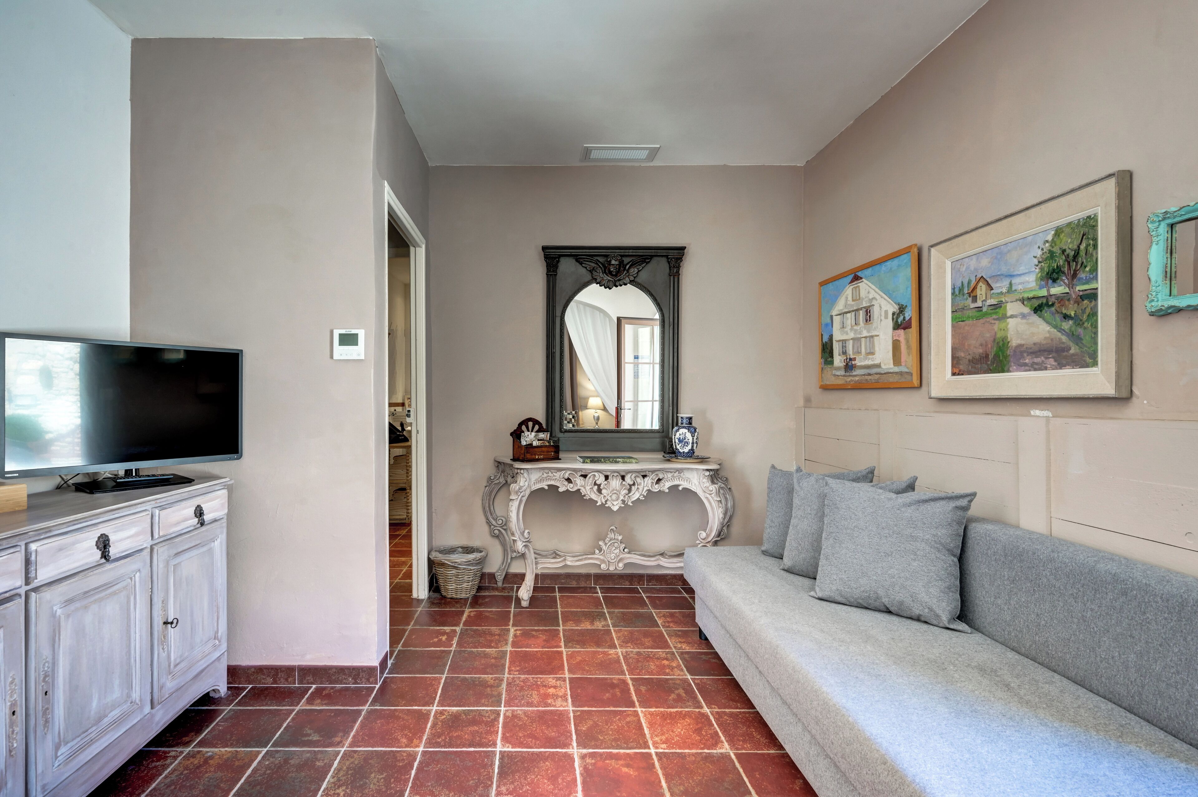 Una sala de estar con televisor, sofá, mesa consola y espejo.