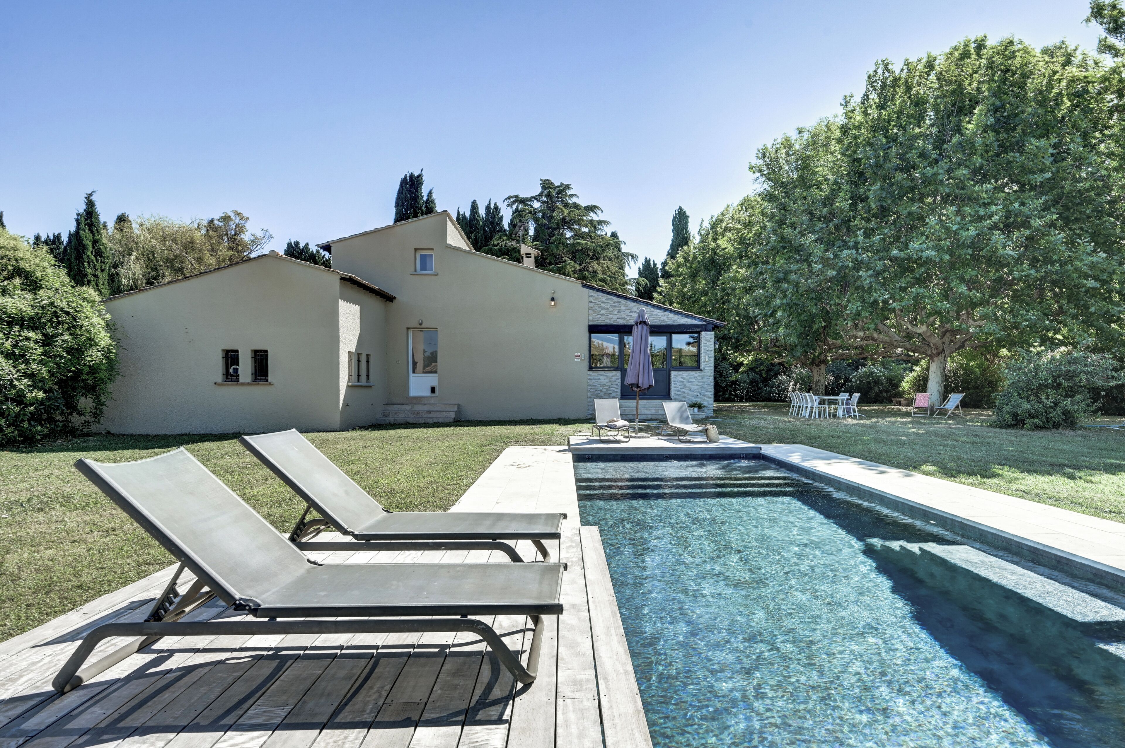 Una piscina con sillas de descanso, una zona de estar cubierta y una casa al fondo.