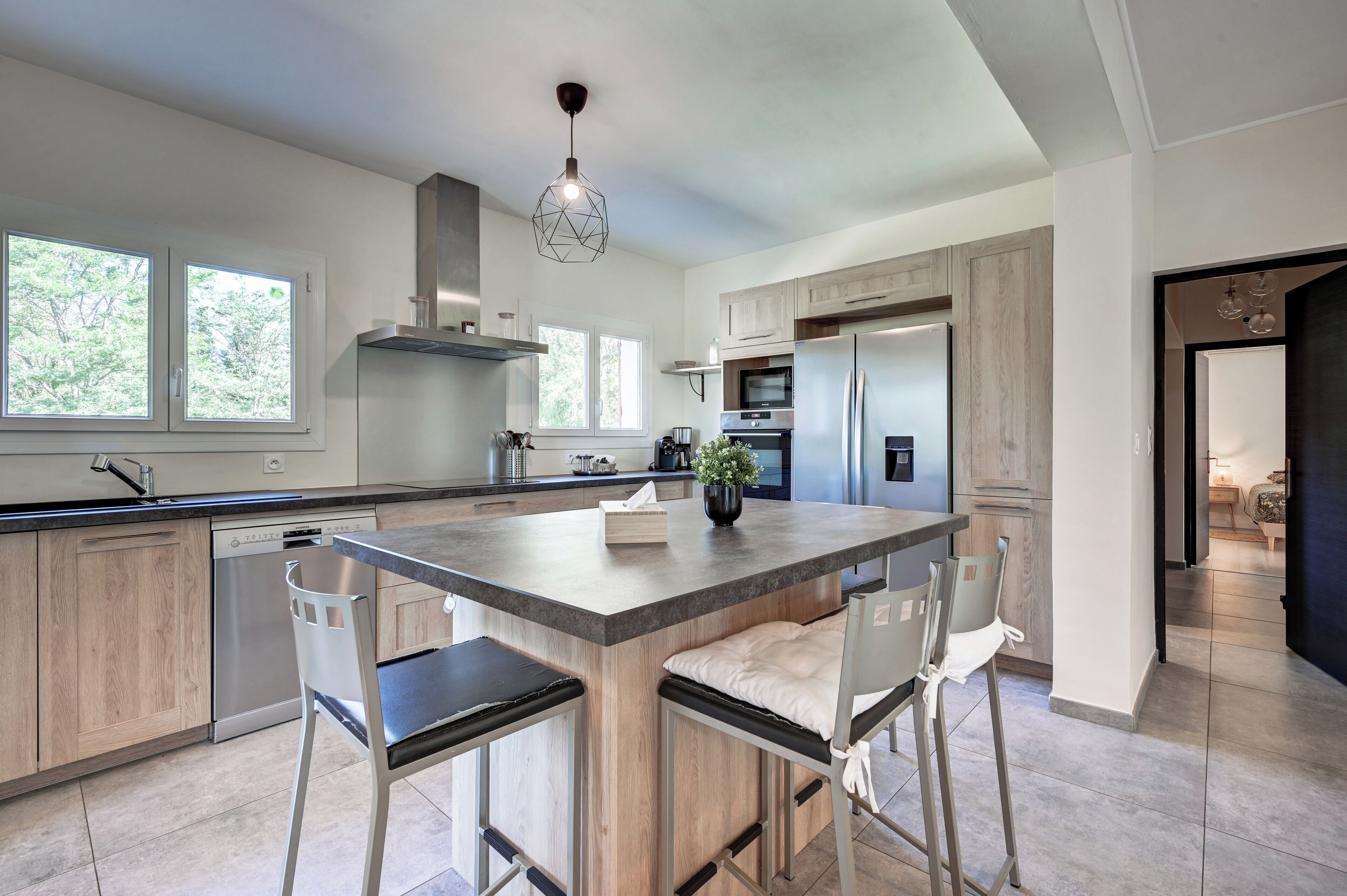 A modern kitchen with a central island, stainless steel appliances, and a view of the outdoors.