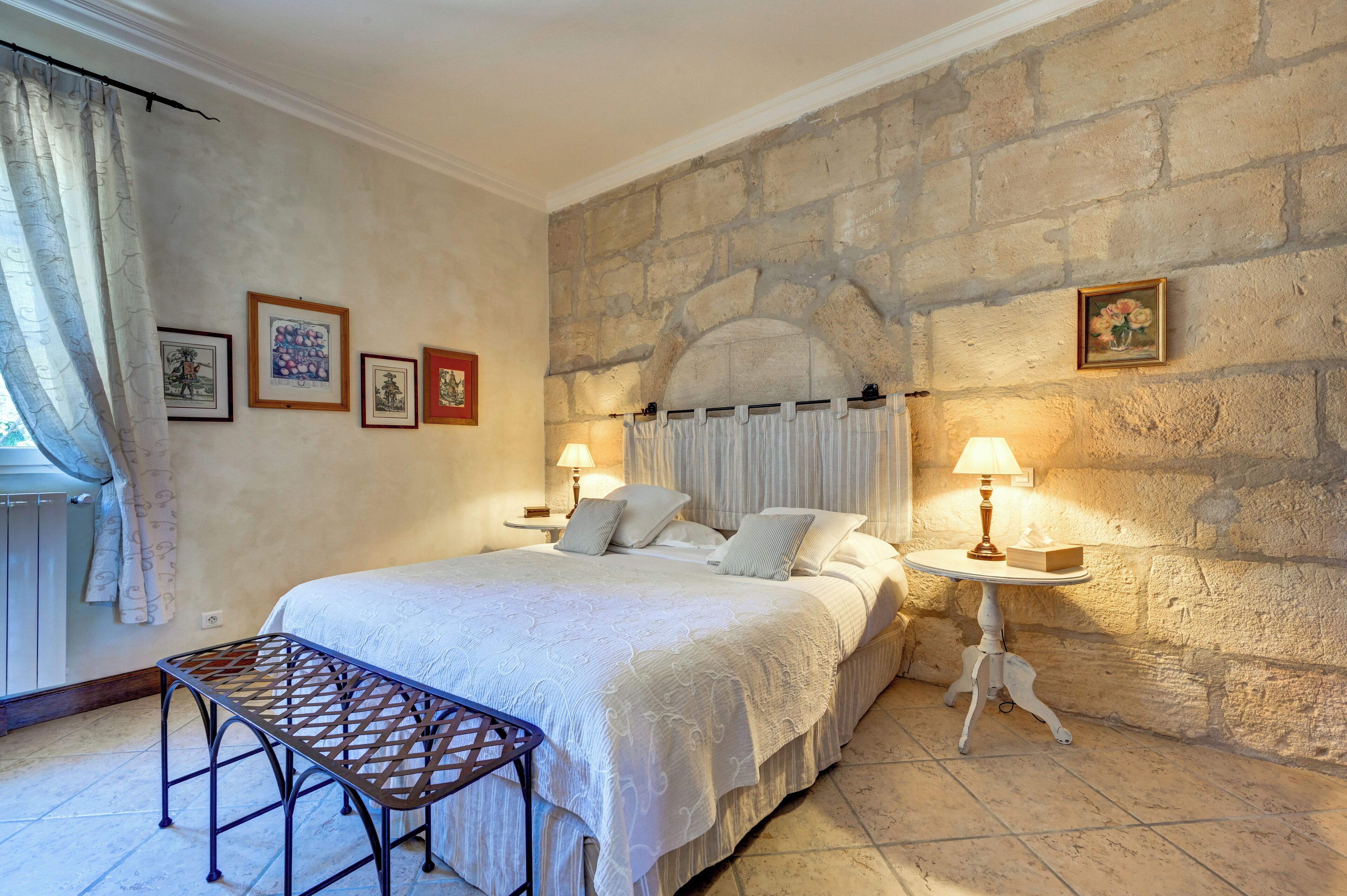 Une chambre avec un mur en pierre, un lit avec une literie blanche, deux lampes de chevet et une petite table avec une lampe.