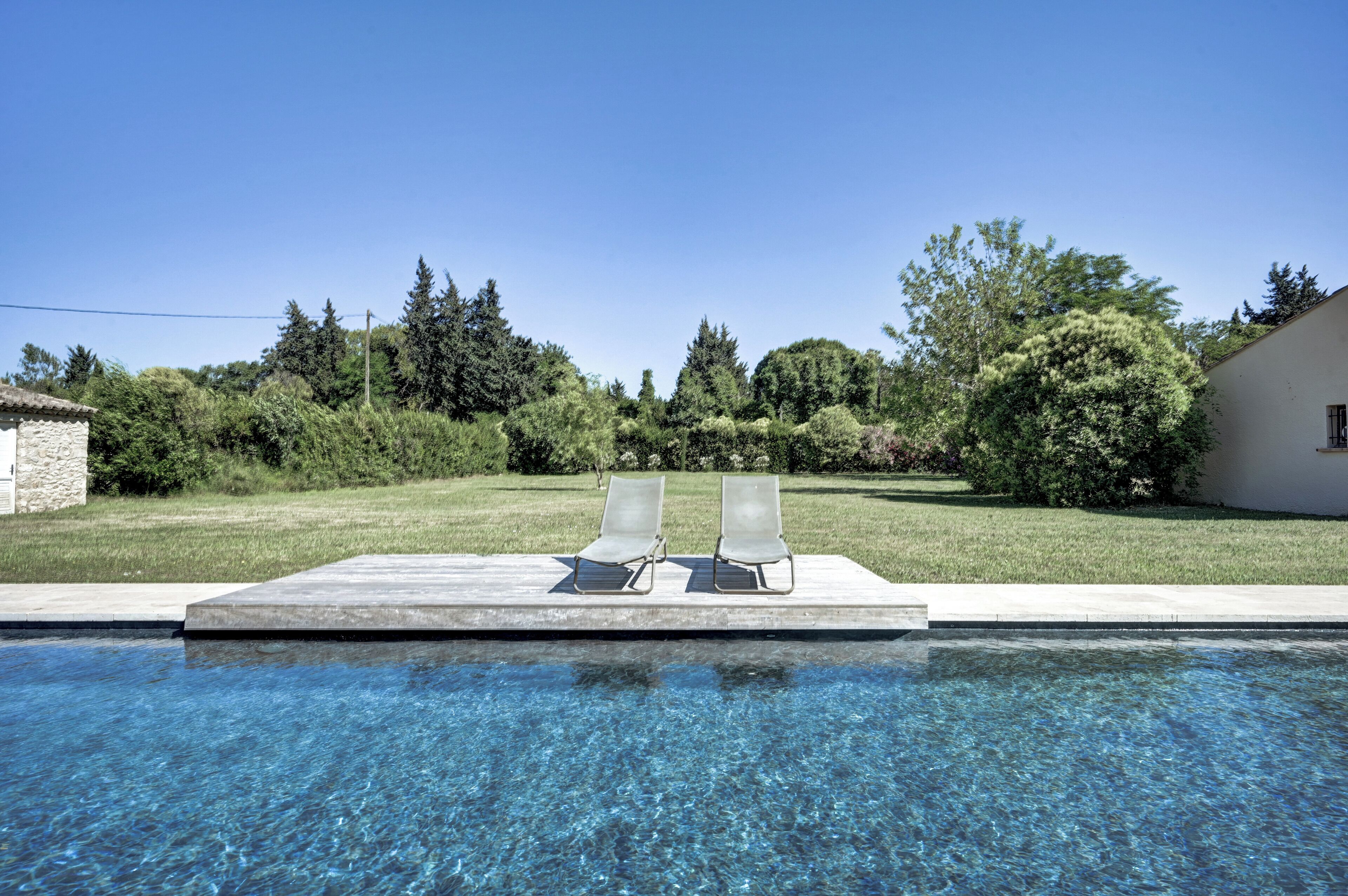 Una piscina con dos sillas reclinables y un muro de piedra.