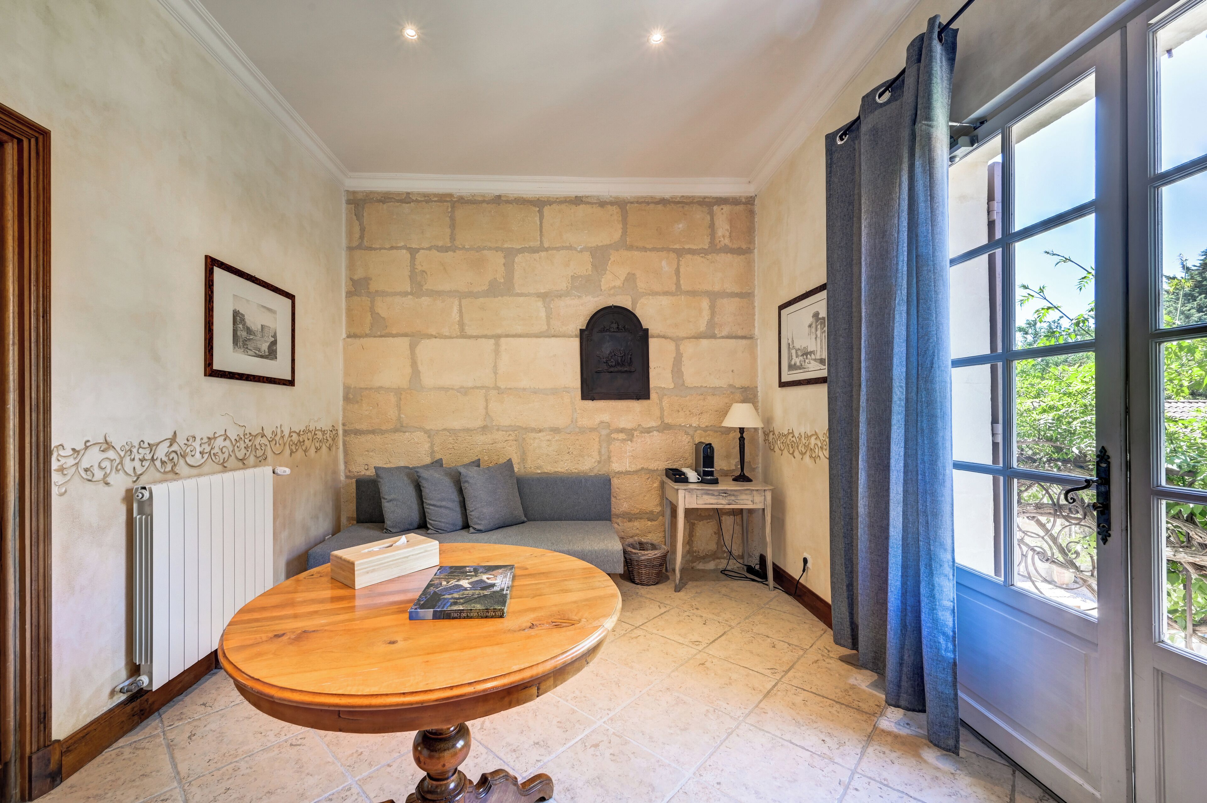 Una habitación acogedora con una pared de piedra, una mesa redonda de madera, un sofá y vistas a través de una ventana con cortinas.