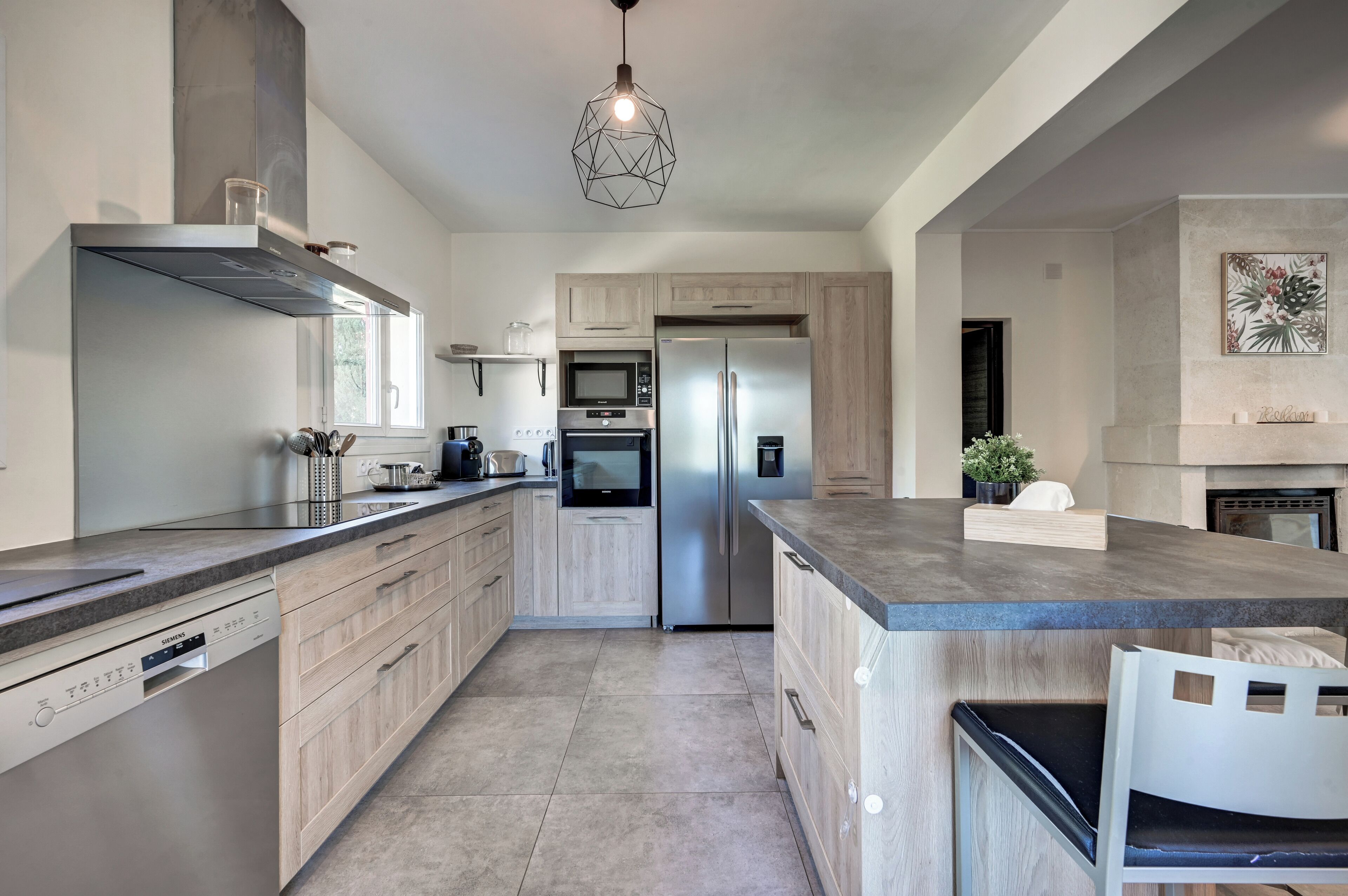 Una cocina moderna con una isla central, electrodomésticos integrados y una lámpara colgante.