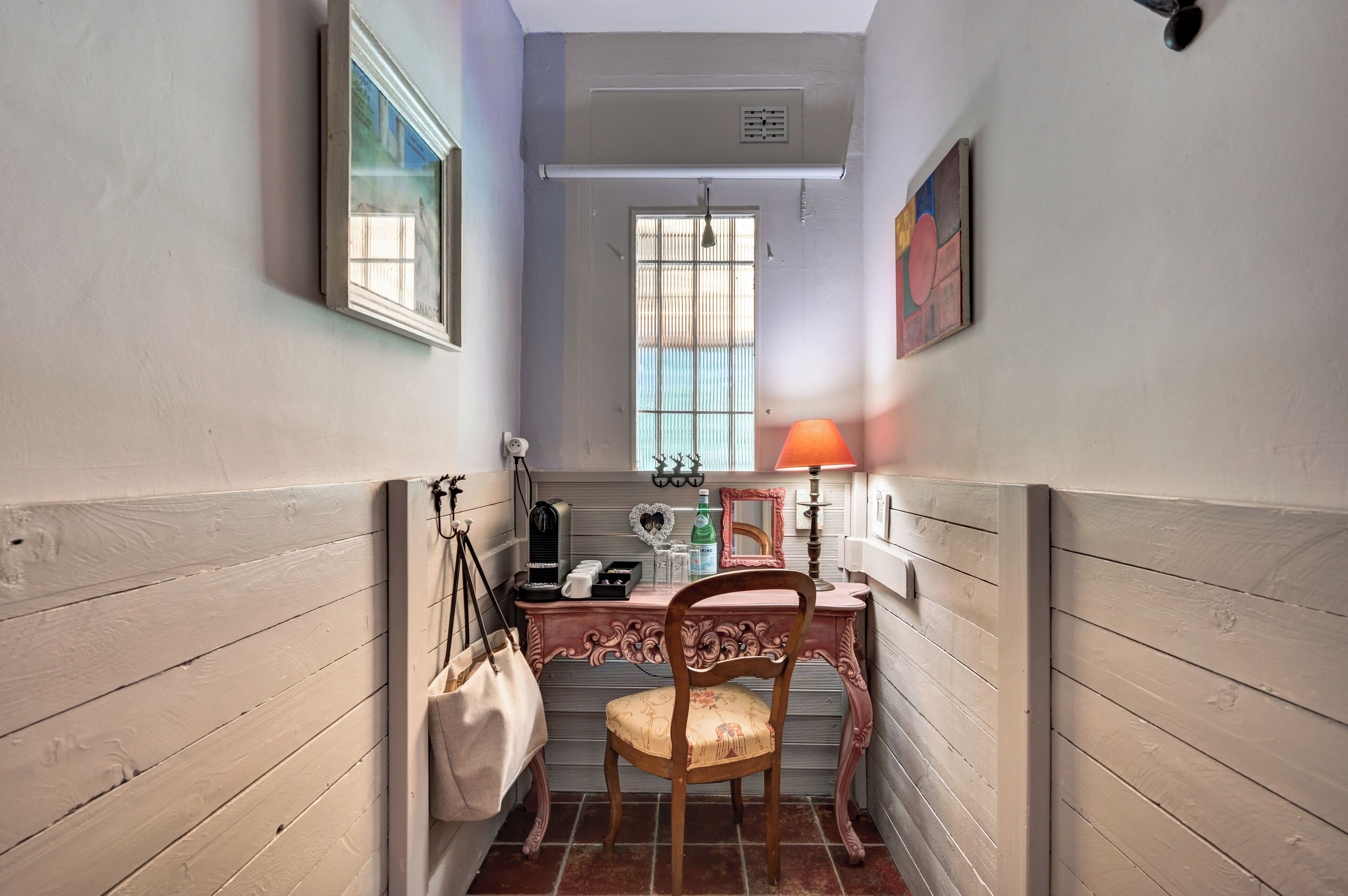 A narrow hallway with a wooden door, a desk with a lamp, and a chair.