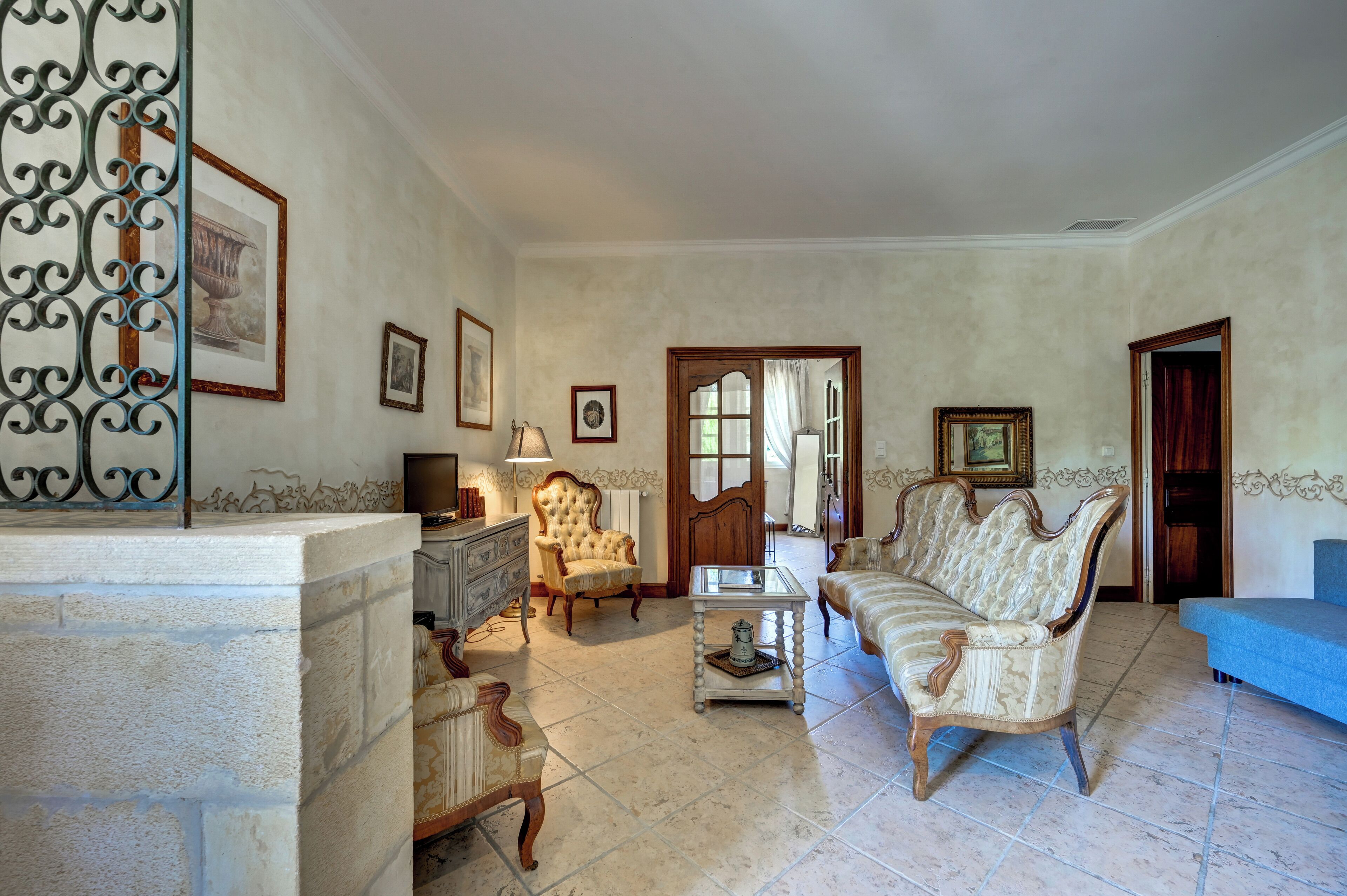 A spacious living room with a sofa, armchair, and a coffee table. There is a fireplace with a decorative screen, a television, and framed artwork on the walls.