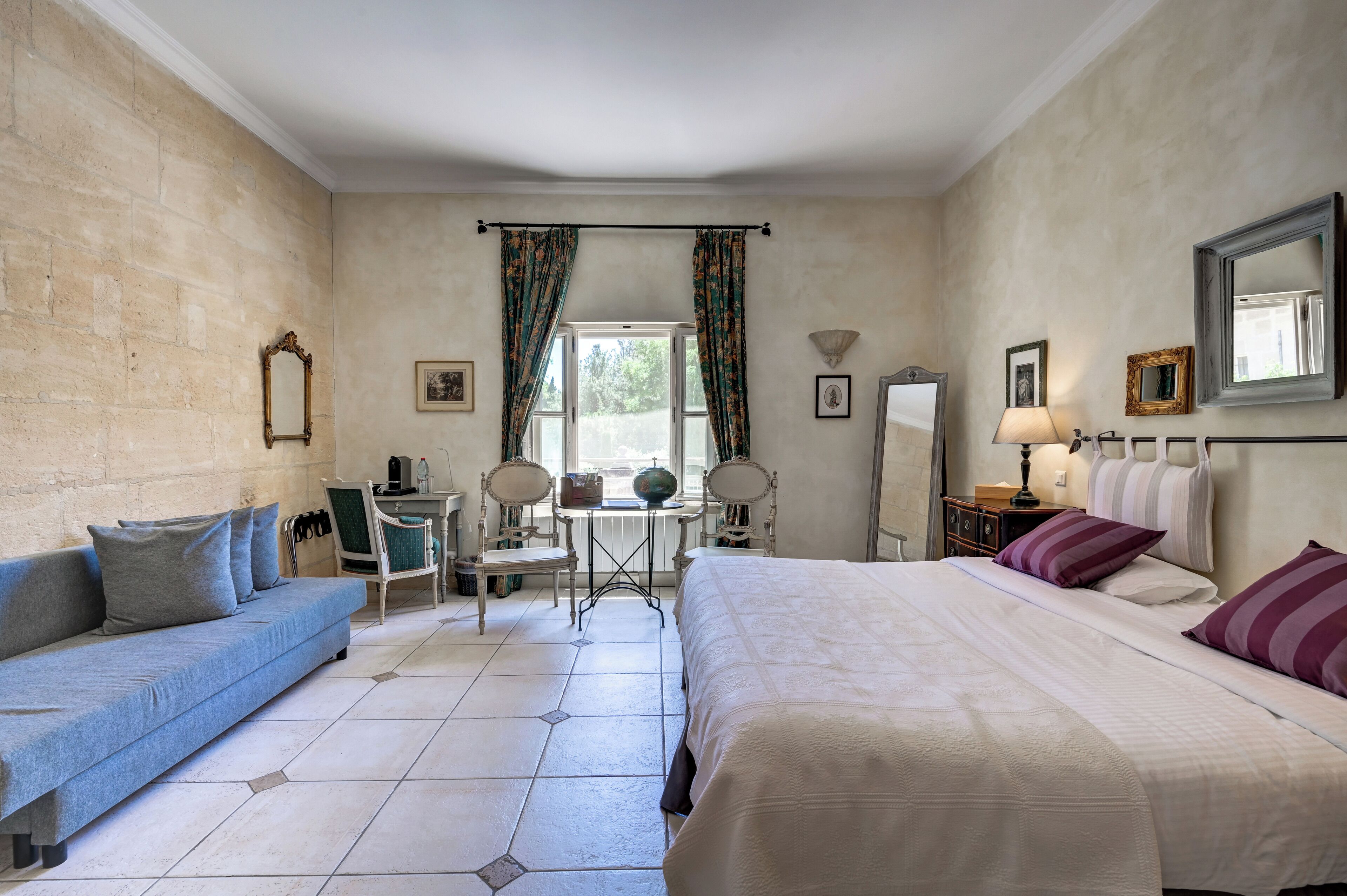 A hotel room with a bed, a sofa, a small table, chairs, and a window with curtains.