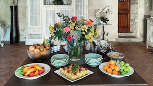 A dining area with a rustic wooden ceiling, a white cabinet with glass doors, and a variety of fruits and flowers on the table. - Mas des Comtes de Provence (Tarascon)