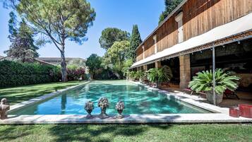 A swimming pool with decorative urns, a wooden building with a covered patio, and lush greenery.