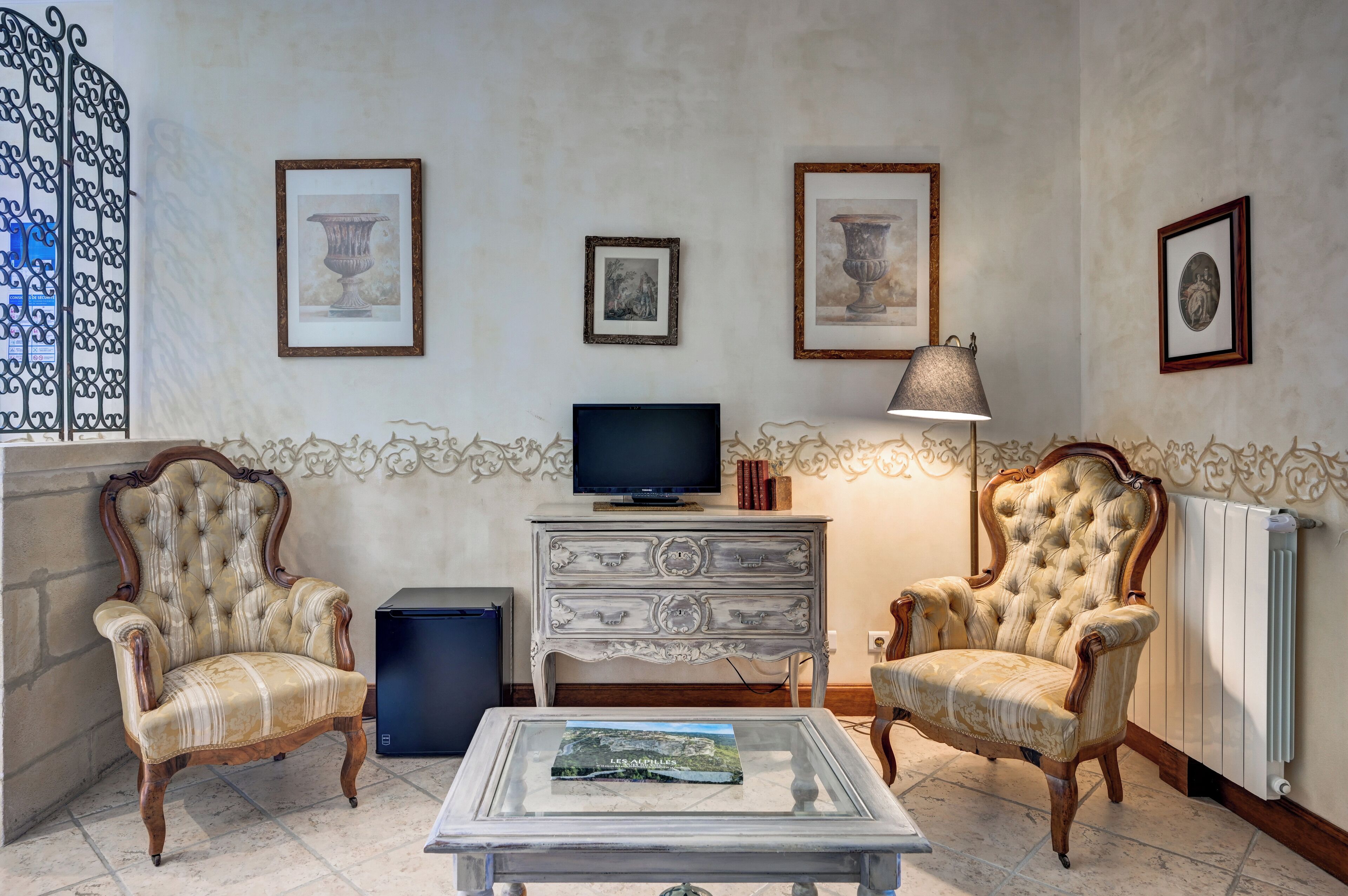 Een woonkamer met twee gestoffeerde fauteuils, een televisie, een bijzettafeltje met een boek en lijstwerken aan de muur.