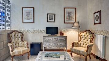 Een woonkamer met twee gestoffeerde fauteuils, een televisie, een bijzettafeltje met een boek en lijstwerken aan de muur.