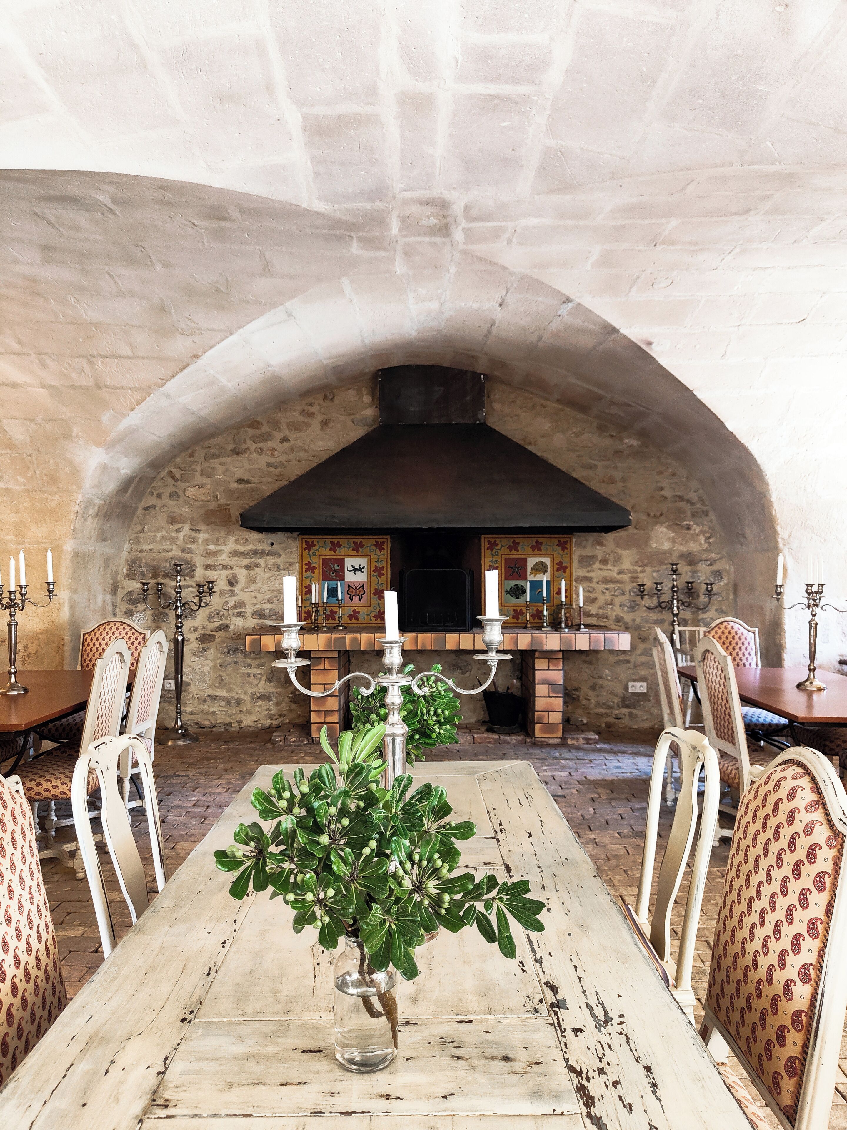 Un comedor rústico con un arco de piedra, una chimenea de ladrillo y una mesa con un jarrón de follaje.