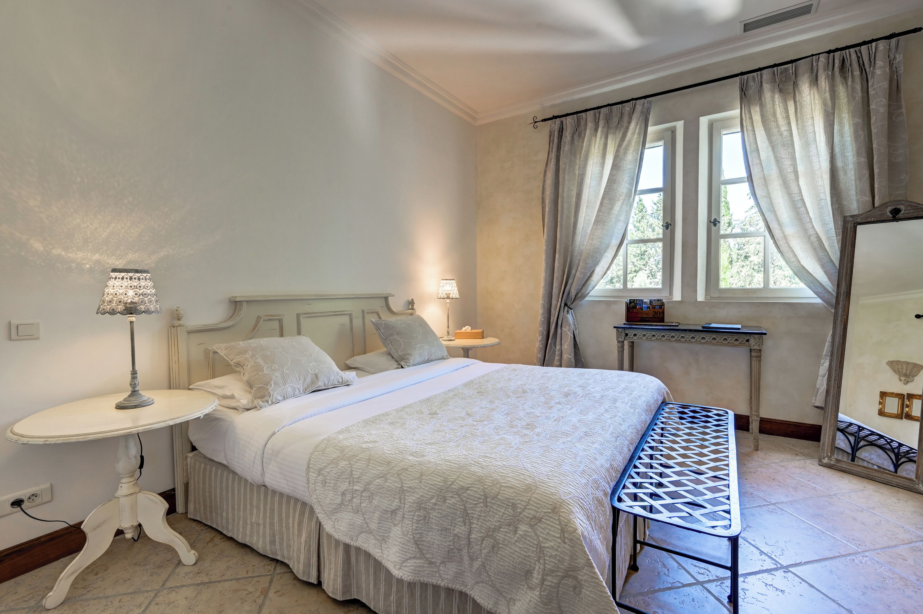 A bedroom with a bed, bedside table, lamp, and a mirror.