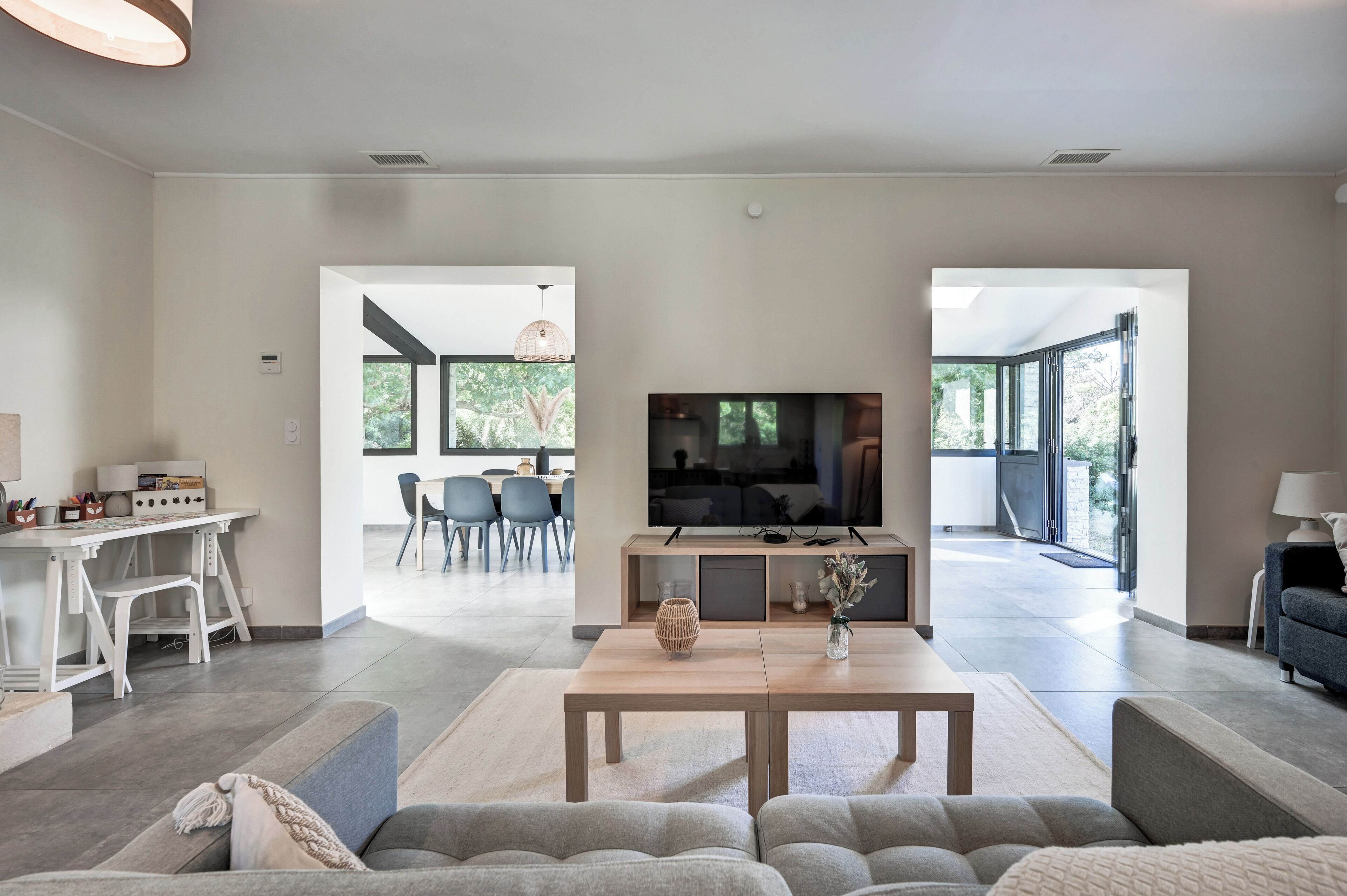 Un salón espacioso con televisor, asientos y un comedor visible a través de una puerta abierta.