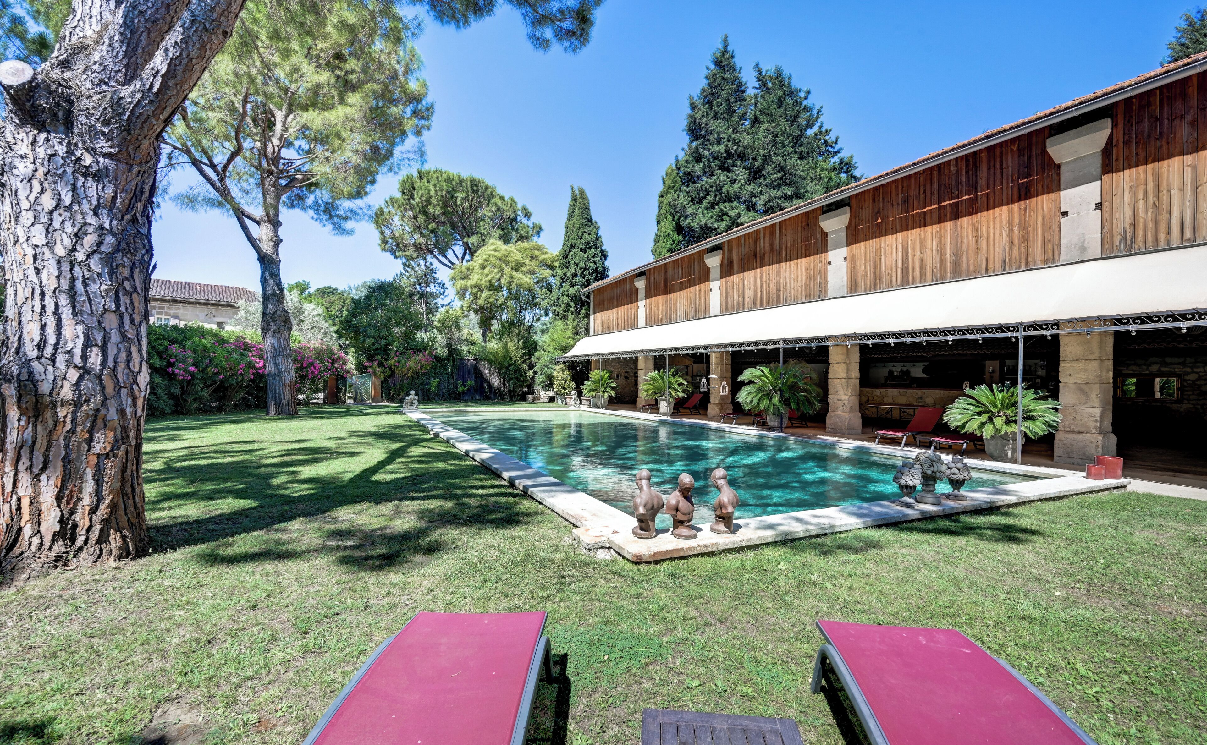 Una piscina con bordo in legno, circondata da un prato curato e alberi.
