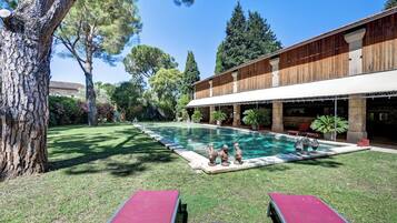 Una piscina con bordo in legno, circondata da un prato curato e alberi.