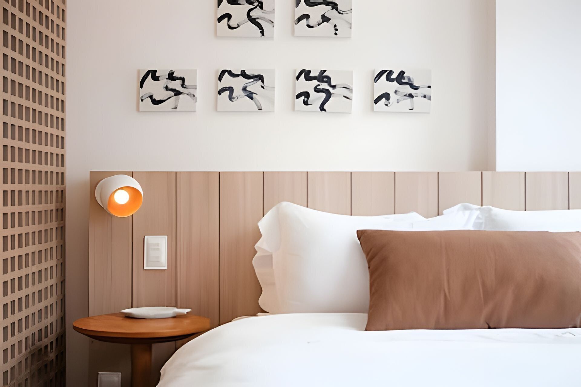 A hotel room with a bed, a nightstand, a wall-mounted light, and abstract art on the wall.