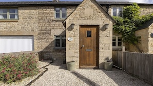 Une maison en pierre avec une porte en bois, une petite fenêtre et une allée gravillonnée.