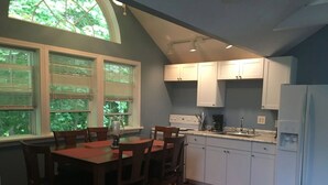 A kitchen with white cabinets, a dining table with chairs, and a refrigerator. - Songbrook + (Otego)