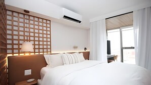 A hotel room with a large bed, a nightstand, a wall-mounted air conditioner, a wooden partition with a grid pattern, and a large window with curtains. - Leblon | Loft 5 min da Praia, com varanda vista Cristo - por Casapē Rio (Rio de Janeiro)