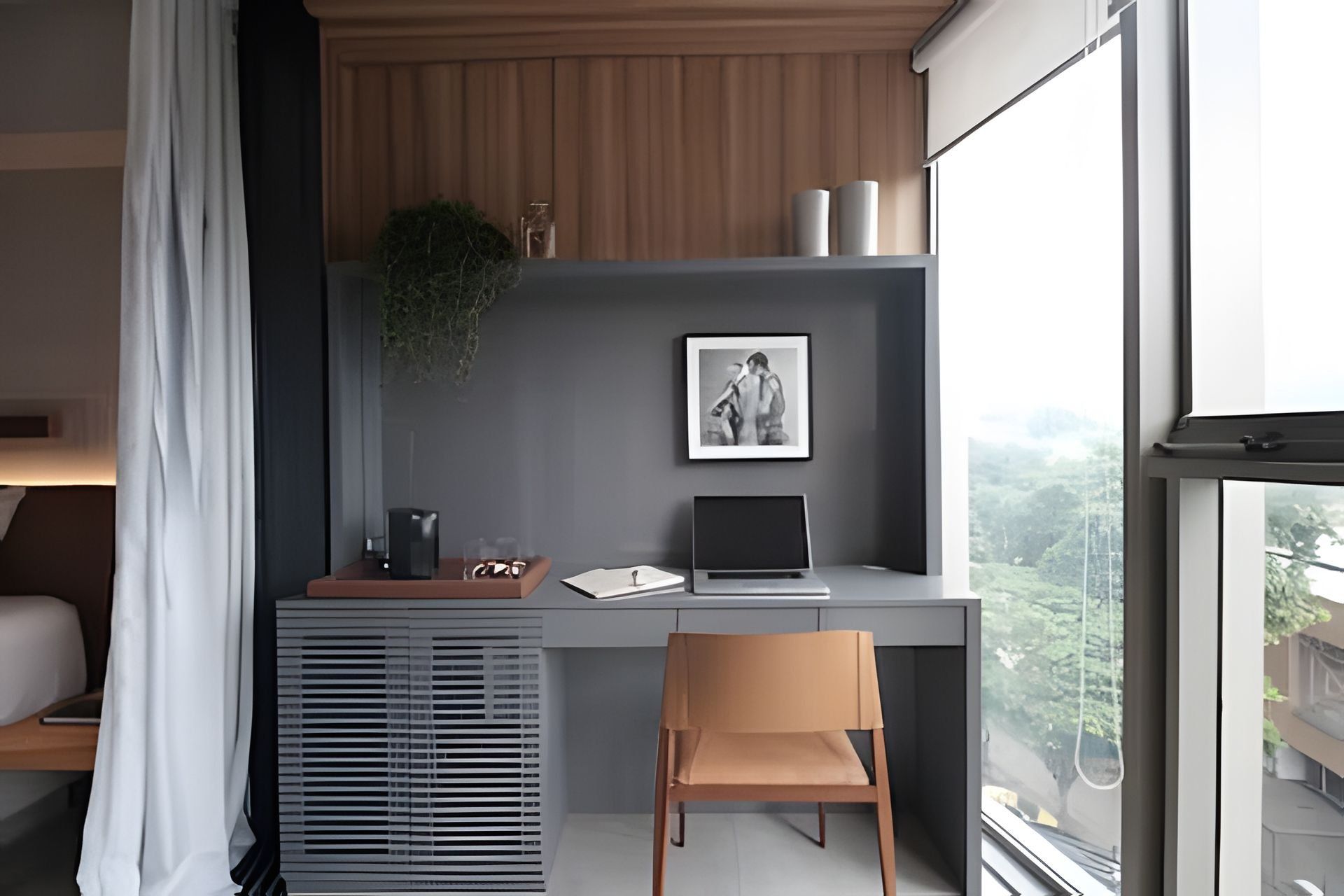 A modern office space with a desk, laptop, and chair, a framed picture on the wall, and a window with a view of greenery.