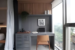 Un espacio de oficina moderno con un escritorio, una laptop, una silla, un cuadro en la pared y una ventana con vista a zonas verdes.