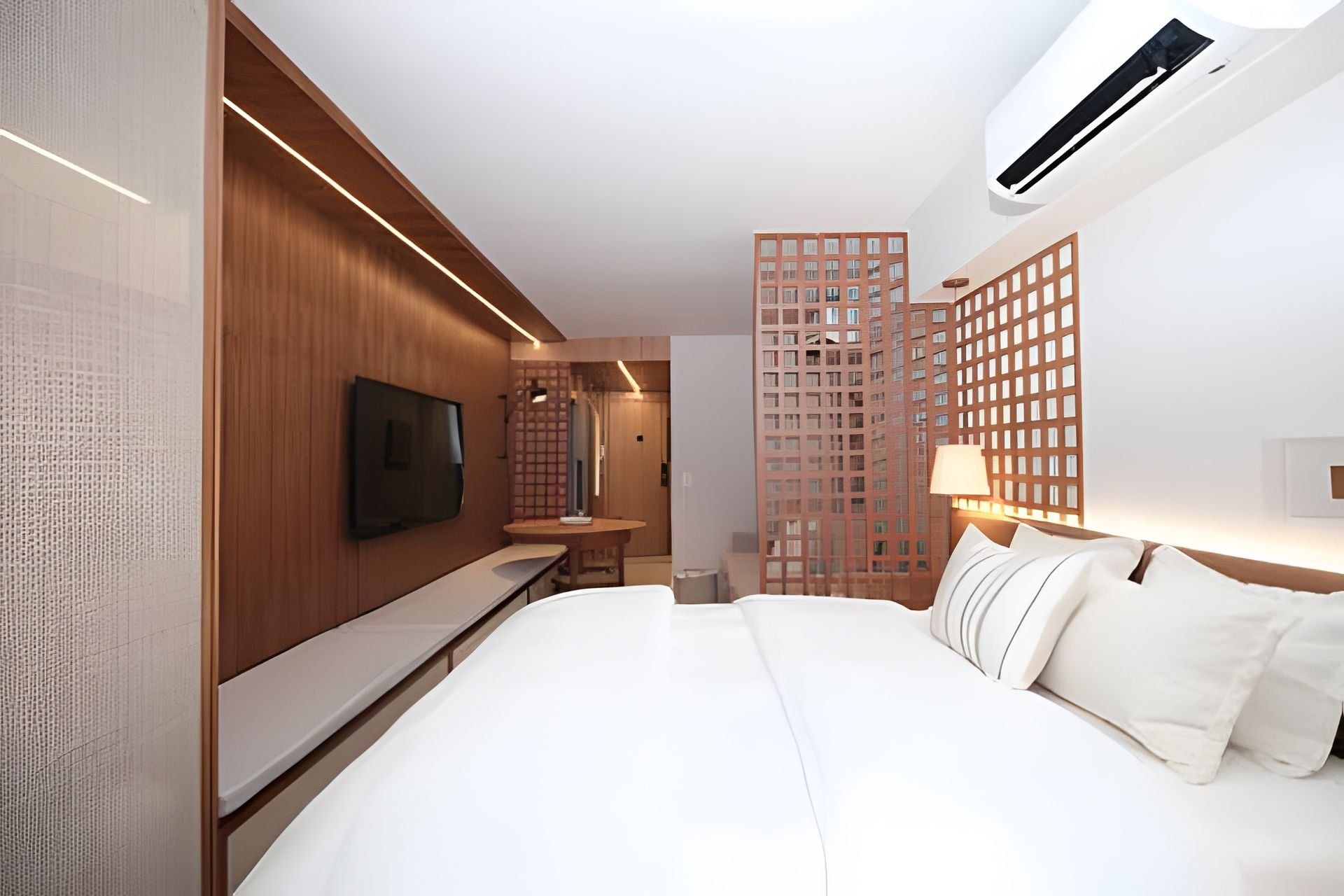 Une chambre d’hôtel moderne avec un grand lit, un téléviseur à écran plat fixé au mur, un décor avec des panneaux en bois et une vue sur un immeuble de grande hauteur.