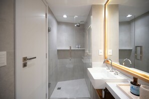 Un baño moderno con cabina de ducha de vidrio, un lavabo blanco con encimera de madera y un espejo grande.