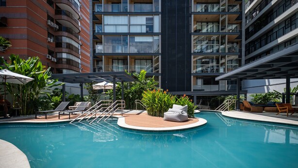 A modern pool area with lounge chairs and a small seating area, surrounded by tall buildings. - Leblon | Loft 5 min da Praia, com varanda vista Cristo - por Casapē Rio (Rio de Janeiro)