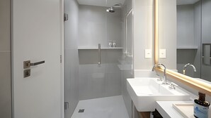 A modern bathroom with a glass shower enclosure, a white sink, and a large mirror. - Leblon | Loft 5 min da Praia, com varanda vista Cristo - por Casapē Rio (Rio de Janeiro)