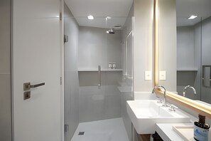 Un baño moderno con cabina de ducha de vidrio, un lavamanos blanco y un espejo grande.