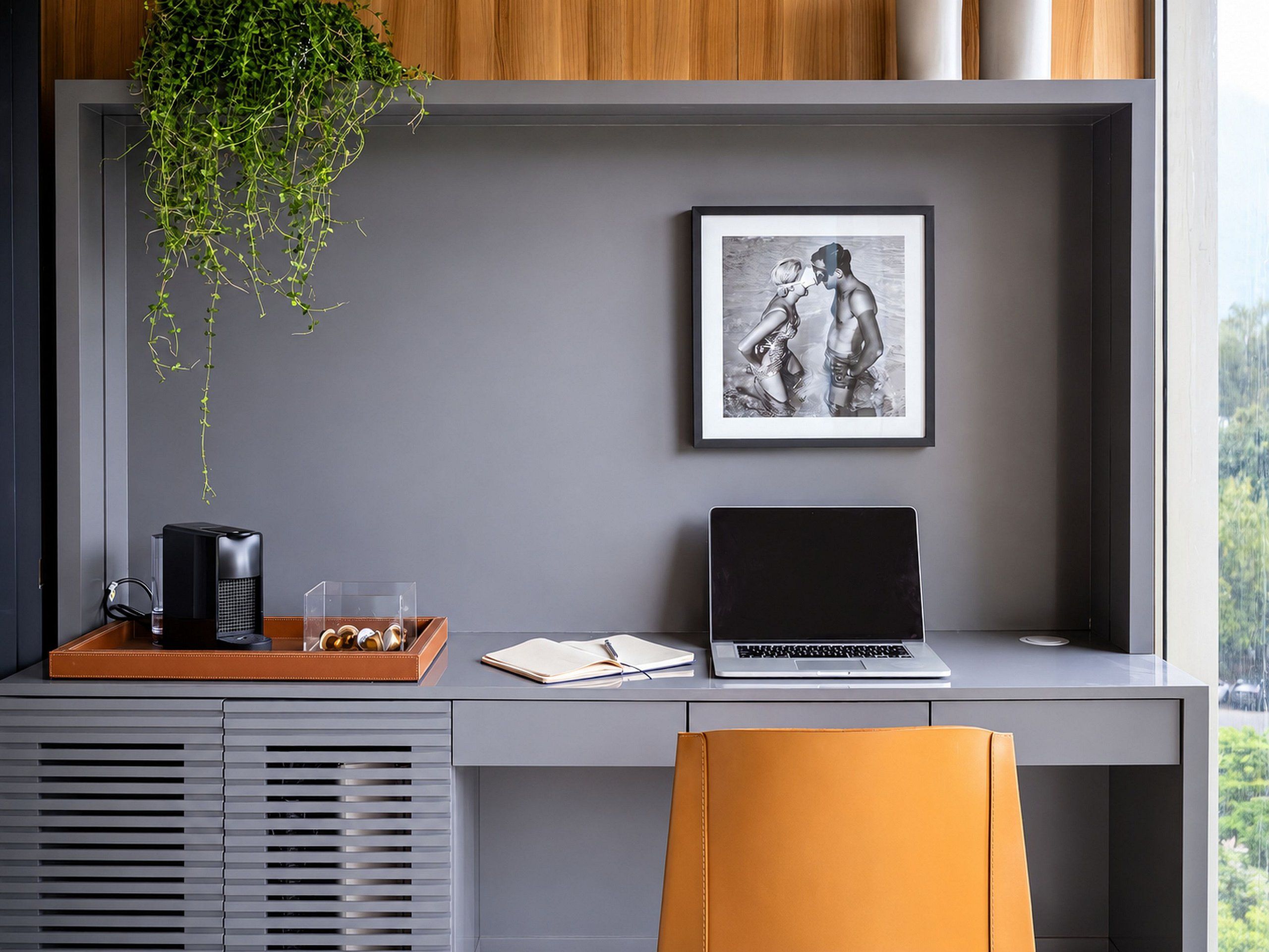 A modern workspace with a laptop, a framed picture, a plant, and a coffee maker on a desk.