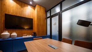 A conference room with a wooden table, blue cabinets, and a large screen. - Leblon | Loft 5 min da Praia, com varanda vista Cristo - por Casapē Rio (Rio de Janeiro)