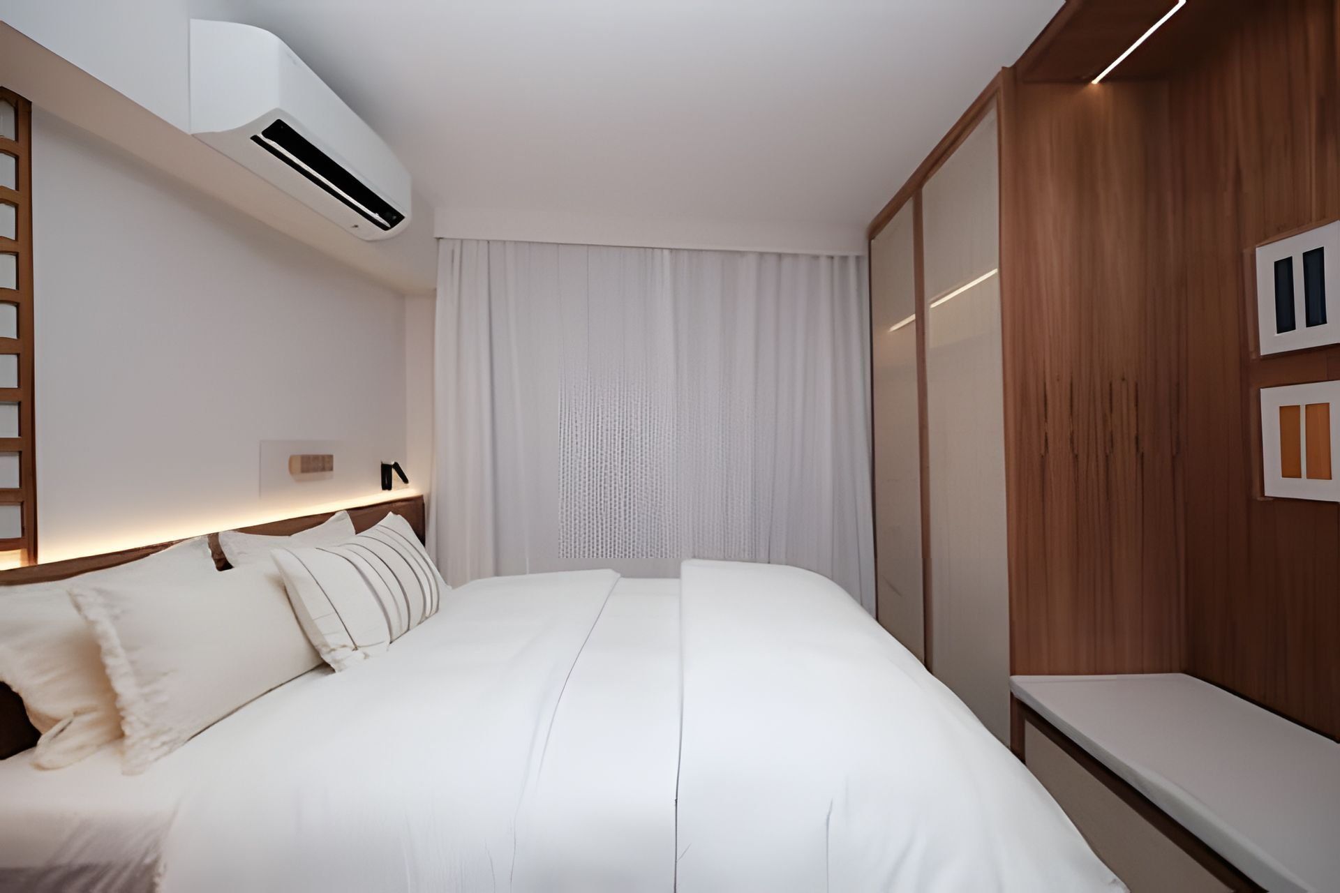 A modern hotel room with a large bed, an air conditioning unit, a bedside table, and a wooden panel wall.
