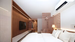Una habitación de hotel moderna con una cama grande, un televisor de pantalla plana montado en la pared, detalles de paneles de madera y vista a un edificio alto.