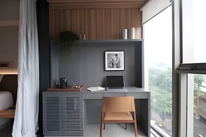 Un espacio de oficina moderno con un escritorio, una laptop, una silla, un cuadro en la pared y una ventana con vista a zonas verdes.