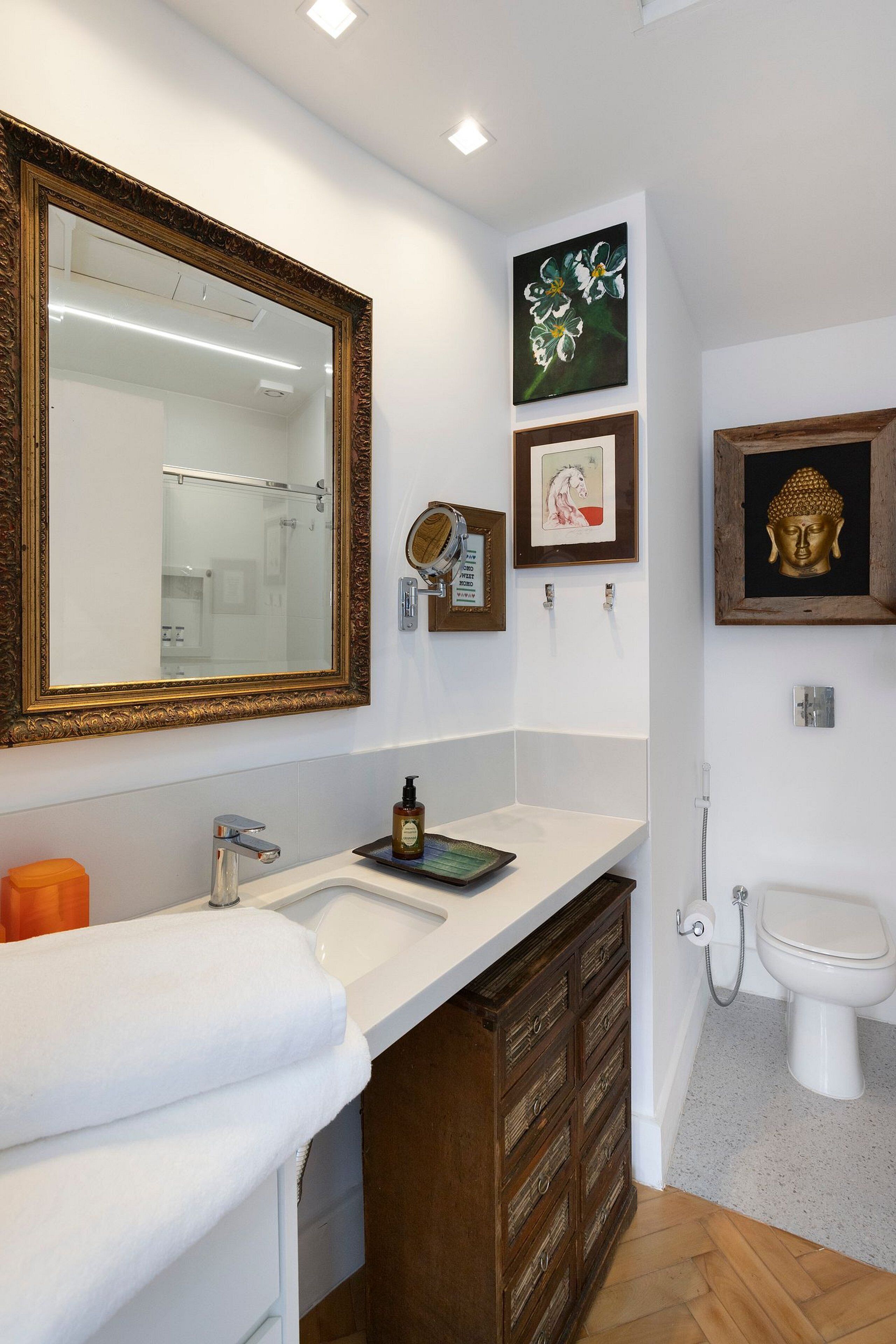 A bathroom with a large mirror, a sink, a toilet, and decorative wall art.