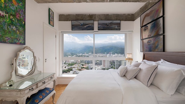 Een slaapkamer met een groot bed, een dressoir, een spiegel en kunstwerken aan de wanden.