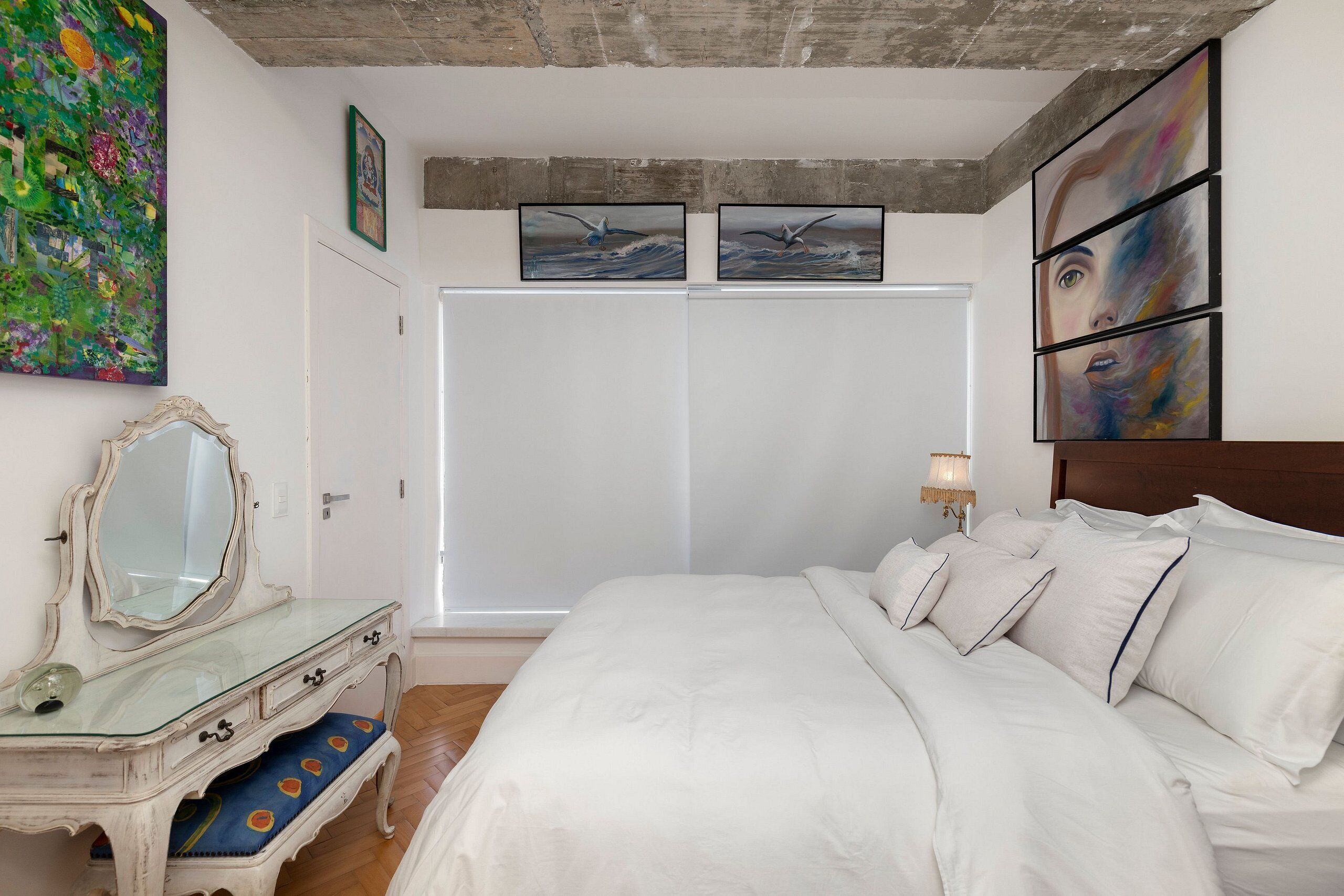 A bedroom with a large bed, a dresser, a wardrobe, and artwork on the walls.