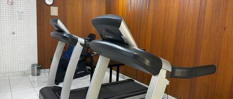 Une salle de sport équipée de tapis de course et d’un vélo d’appartement, avec des murs en bois et un sol carrelé.