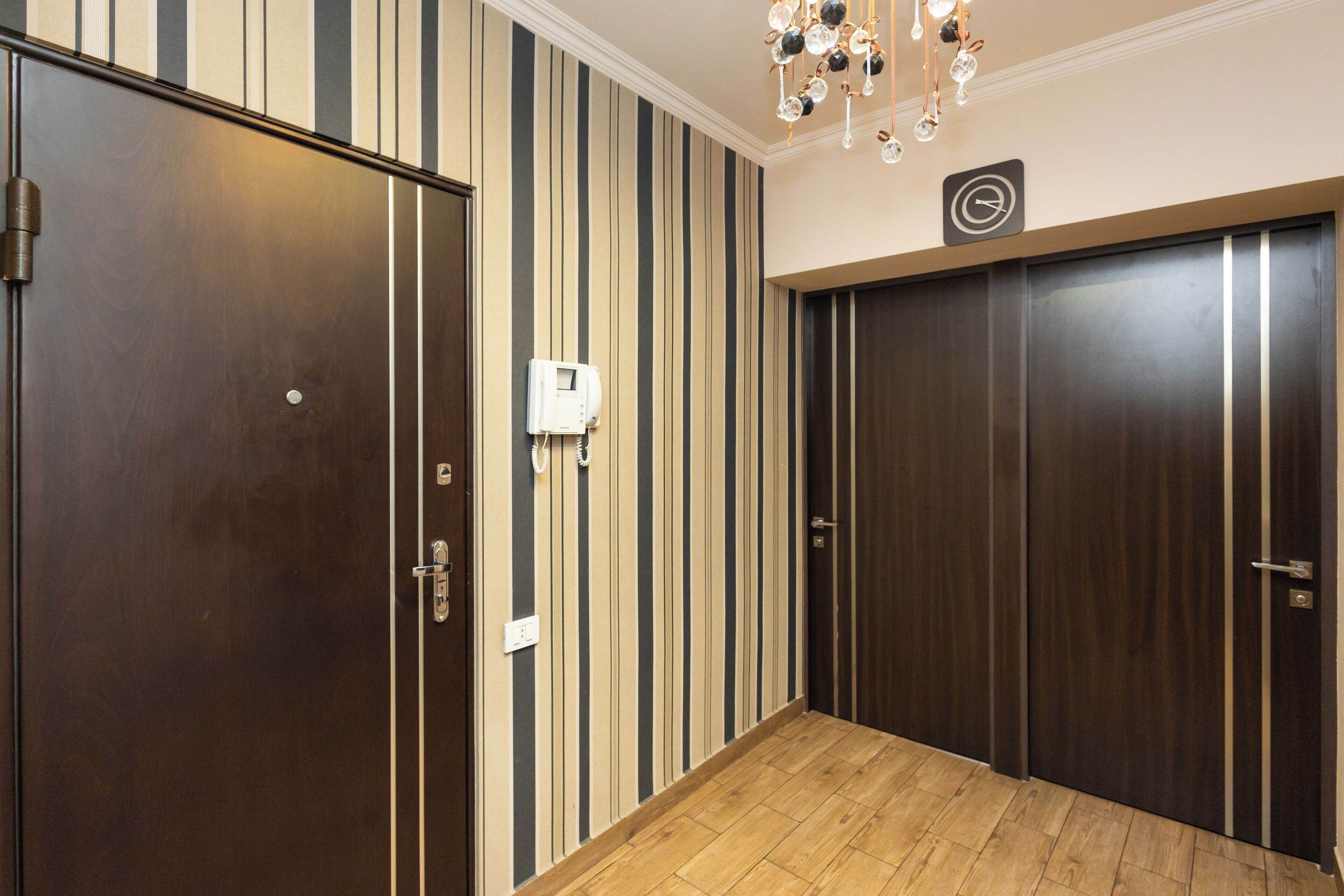 A hallway with striped wallpaper, wooden flooring, and a wall-mounted telephone.
