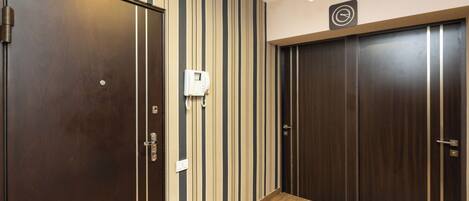 A hallway with striped wallpaper, wooden flooring, and a wall-mounted telephone.