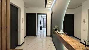 Un pasillo moderno con suelo de mármol, mostrador de recepción de madera y puertas oscuras.